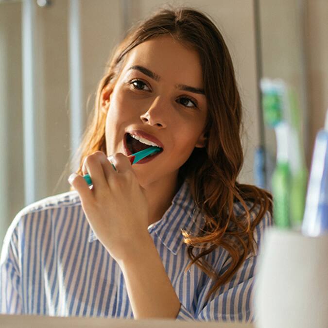 Mujer mirandose al espejo y cepillando sus dientes