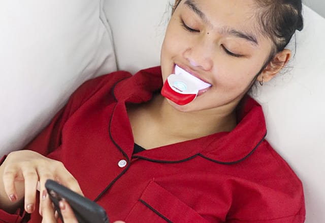 Lady using Colgate's teeth whitening kit while she uses her phone on a sofa