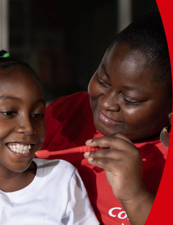Vemos a Gloria, voluntaria de Colgate, enseñándole a una estudiante a cepillarse los dientes.
