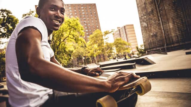 a man smiling sitting down holding a skateboard at a park
