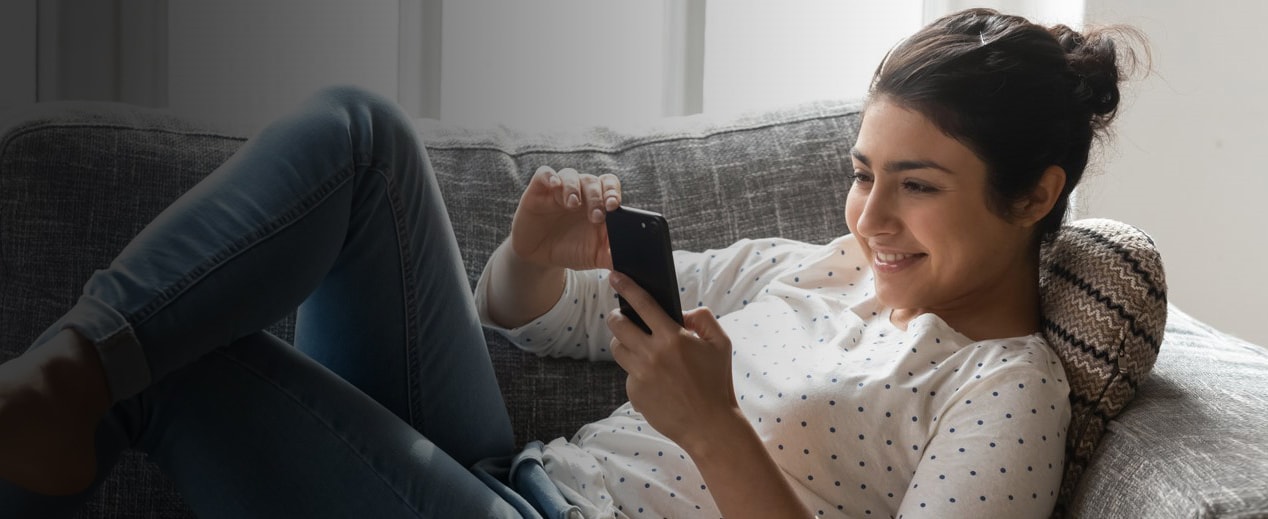 Happy Indian woman relaxing on couch at home, using phone