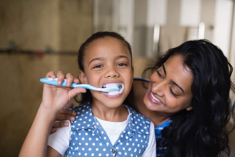 Young girl brushing her teeth with her mom