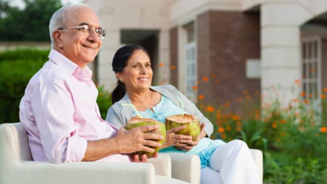 and elderly couple sitting down smiling brightly while holding a coconut