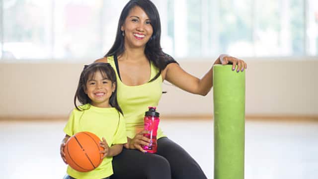 a mother with a yoga mat and daughter holding a basketball smiling brightly