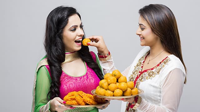 a woman smiling while feeding her friend holding a plate of snacks