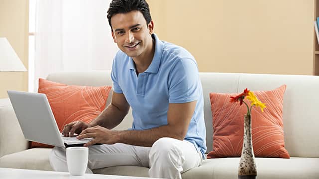 man smiling sitting down on the sofa with a laptop