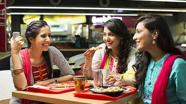 Three women sitting down smiling brightly while enjoying a meal