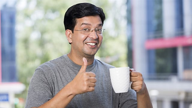 a man smiling while giving a thumbs up and holding a cup of coffee