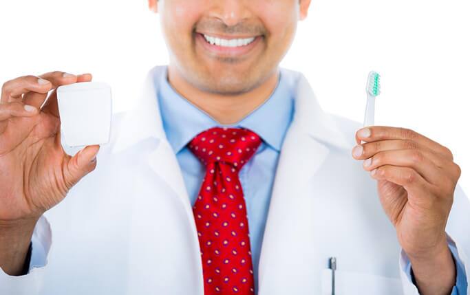 Dentist holding a toothbrush demonstrating sensitive teeth causes