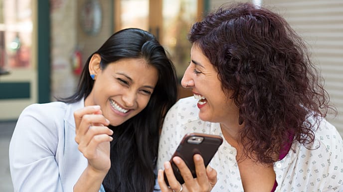 2 women smiling with one of them looking at her phone