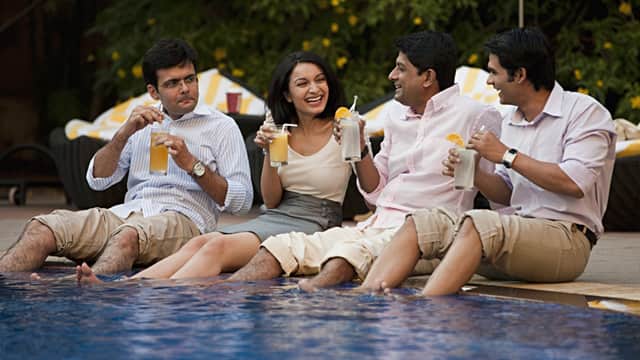 three men and a woman sitting by the pool with their feet dipped in, while enjoying a beverage after work