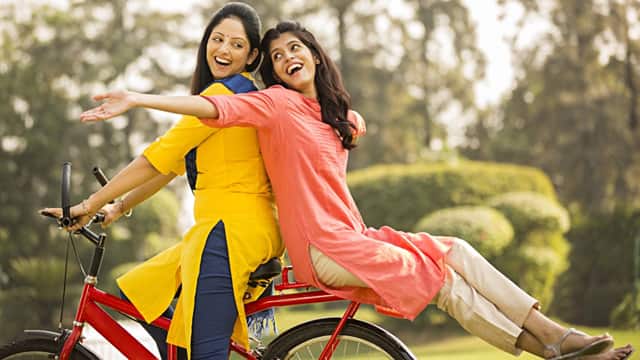 two women smilling while riding a bike