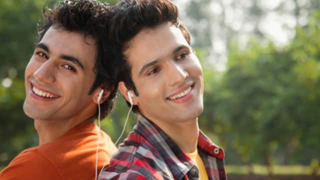 Two men leaning on each other smiling wearing an earphones