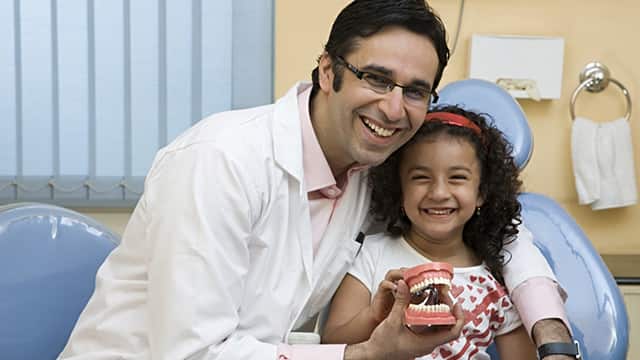 a dentist smiling holding a teeth model nect to a girl patient smiling