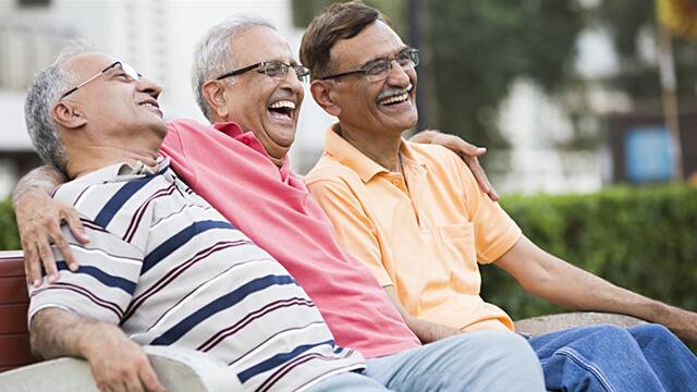 three older men laughing while sitting on a bench