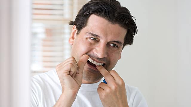 Man noticing plaque on his teeth while looking in the mirror.