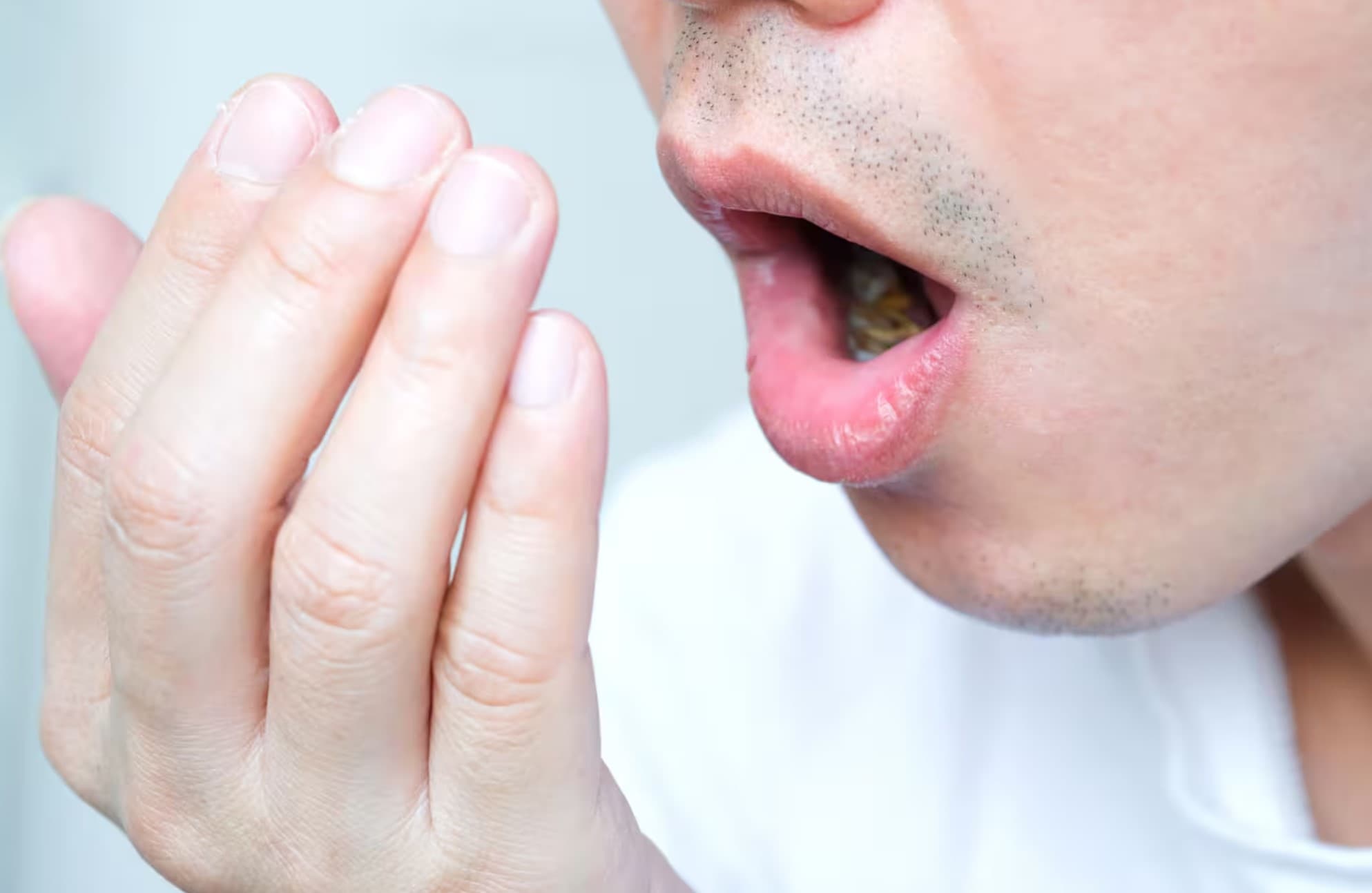 Man checking his breath with his hand, highlighting concerns about dry mouth and bad breath
