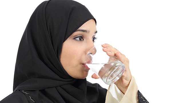 Arab woman drinking water from a glass isolated on a white background