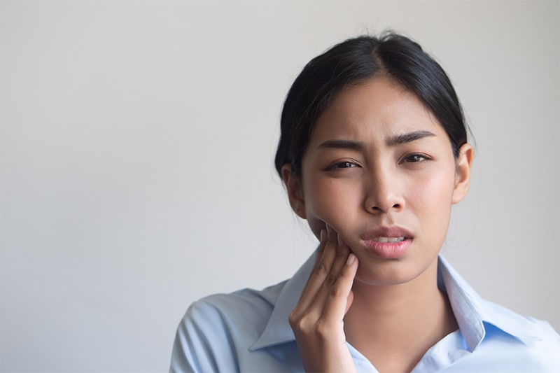 woman holding her cheek in pain, indicating teeth with caries