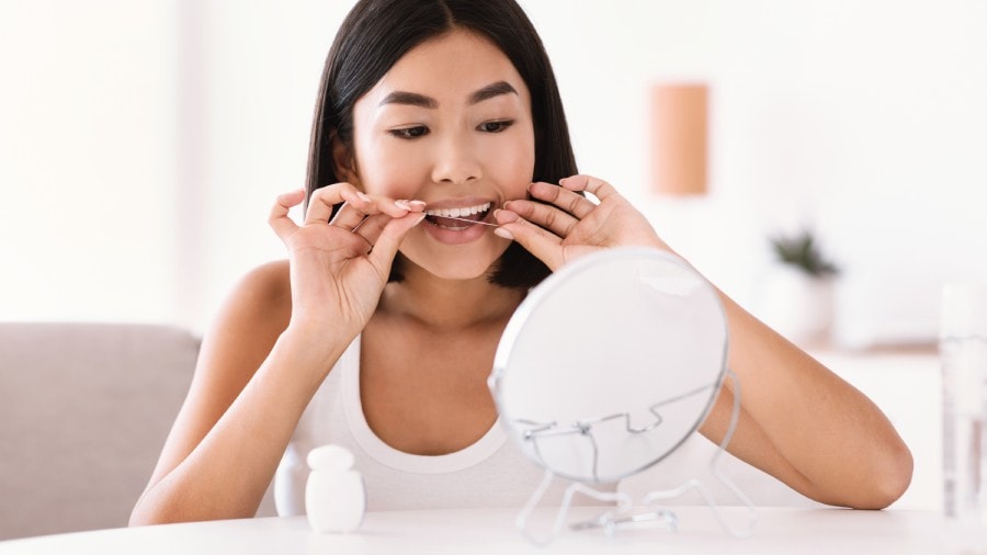 Woman using dental floss in front of a mirror to remove tartar on teeth