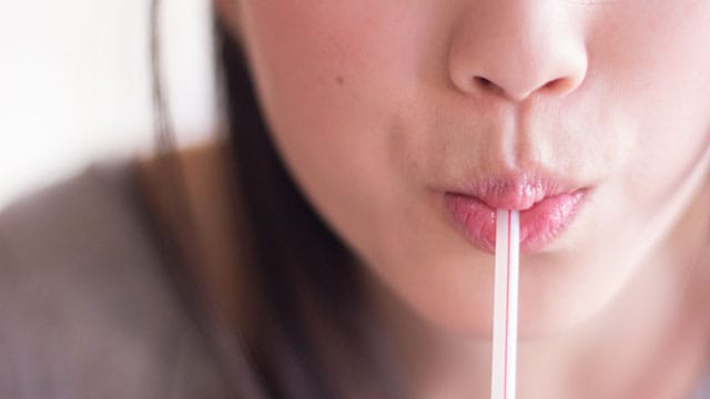 Close-up of a woman sipping a drink through a straw, relieving symptoms of dry mouth