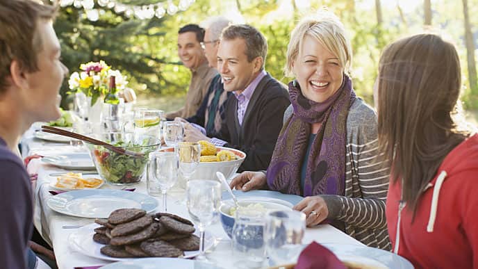 a group of people gathered by the outdoor table smiling while enjoying a feast