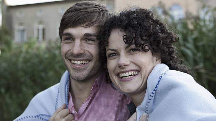 Happy couple wrapped in a blanket sitting outside
