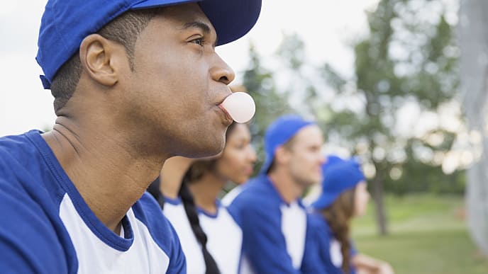 a man blowing a bubble gum while watching outdoor baseball game
