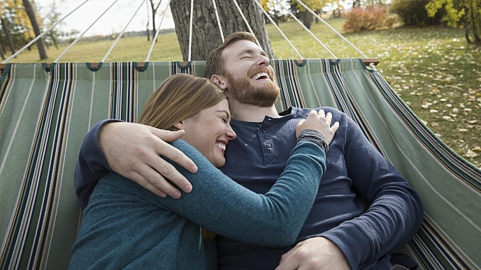 man and a woman laughing while laying on a hammock