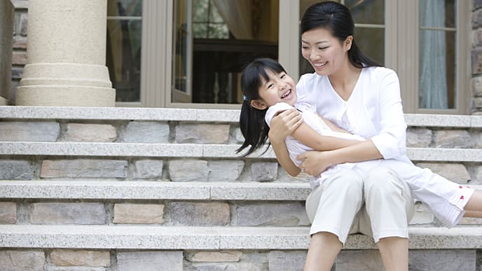 mother sitting down on the step and smiling while holding her daughter
