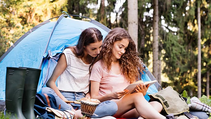 two woman reading a book on a camping site outdoor