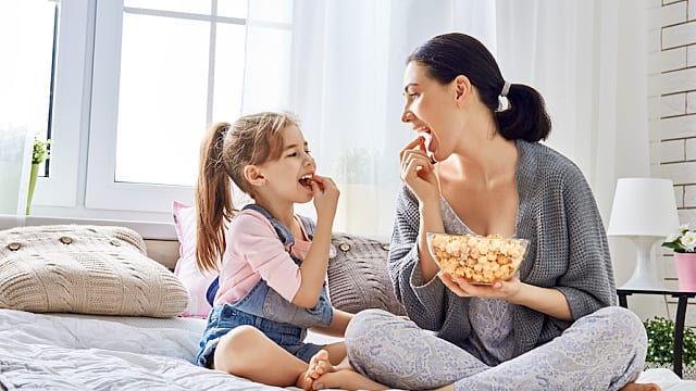 Mother and daughter eating popcorn in bed. 