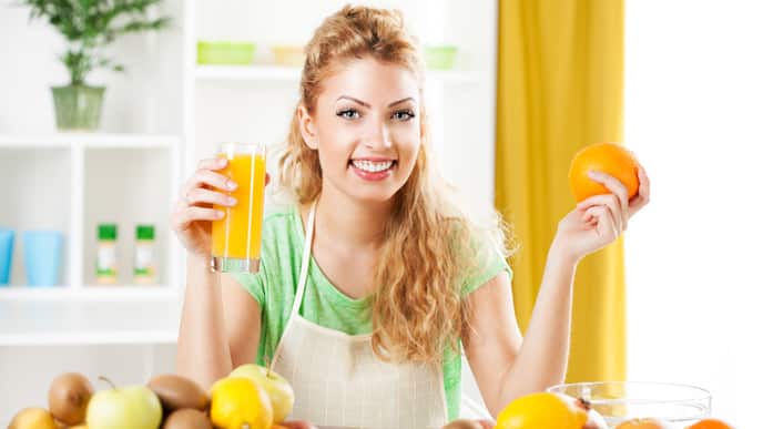 Mujer sonriendo mientras sostiene un vaso y una fruta