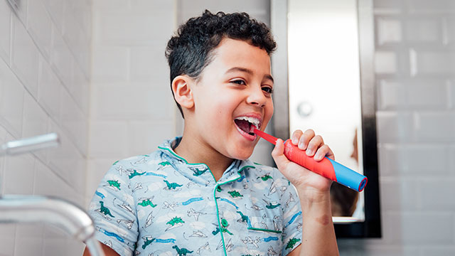 Un infante se cepilla los dientes con un cepillo de dientes eléctrico para niños