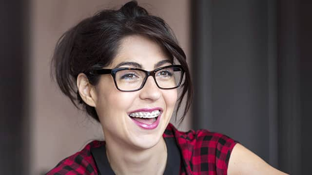 young woman with brown hair and glasses, wearing braces and laughing