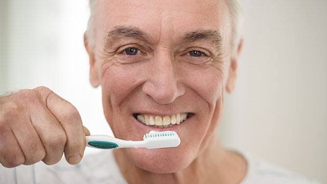 A senior man brushing his teeth in a bathroom