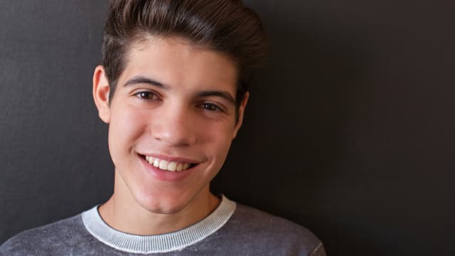 Male teen smiling in a gray shirt against a gray wall