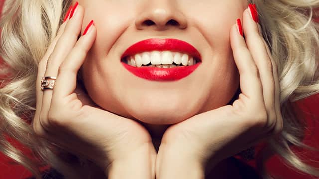 a close up image of a woman wearing red lipstick is smiling with white teeth