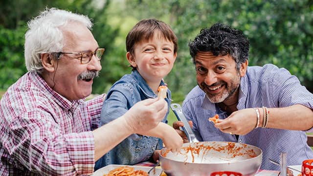 two men and a boy eating out of pan outside