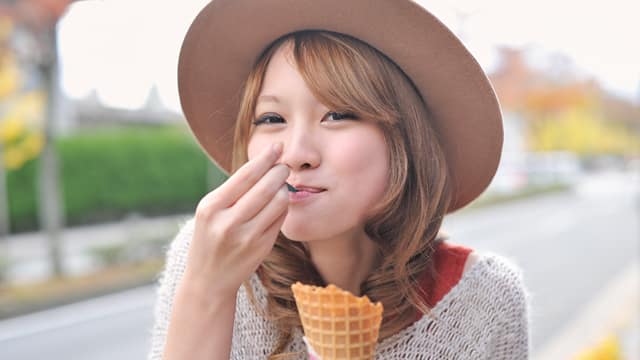 Woman in sweater and hat eating ice cream outside
