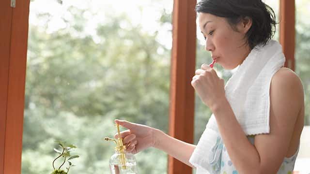 A young woman is brushing her teeth and watering the plant