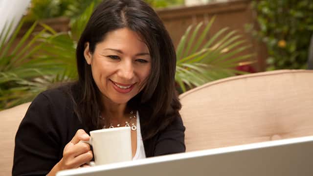 A woman is drinking coffee and looking at the computer screen
