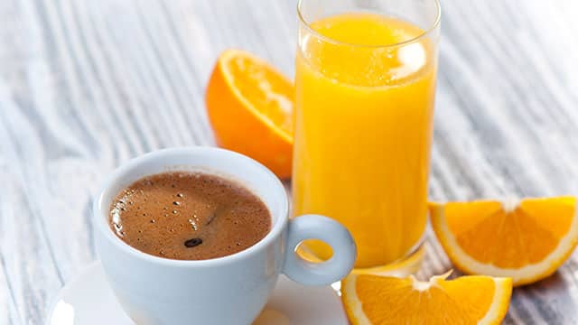 An image of the cup of black coffee, orange juice and orange slices