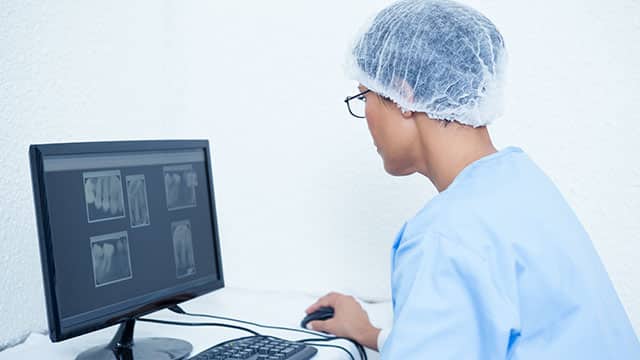 A female dentist is reviewing x-rays on computer screen