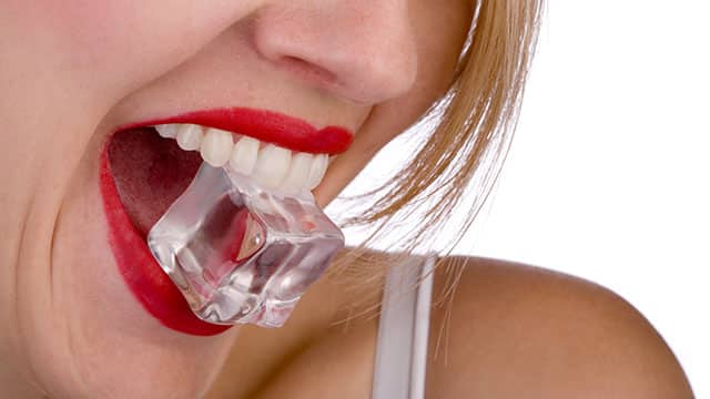 A close up of woman's face with the ice cube in her mouth
