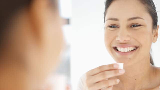 Woman smiling in mirror holding mouthwash