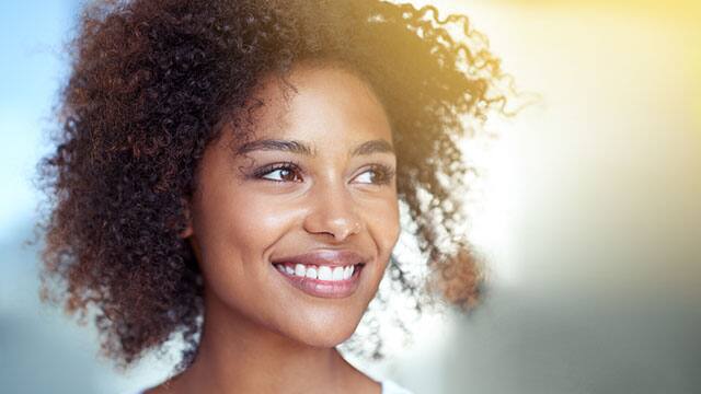 woman smiling after having braces taken off with a sunbeam in the background