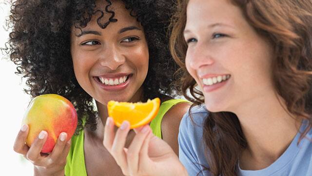 Two young women eating fruit and smiling 