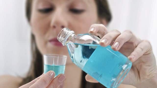 A woman pouring mouthwash into a small cup