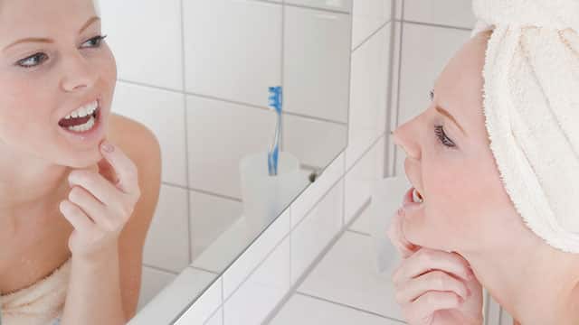 Young woman is looking at her mouth in the mirror